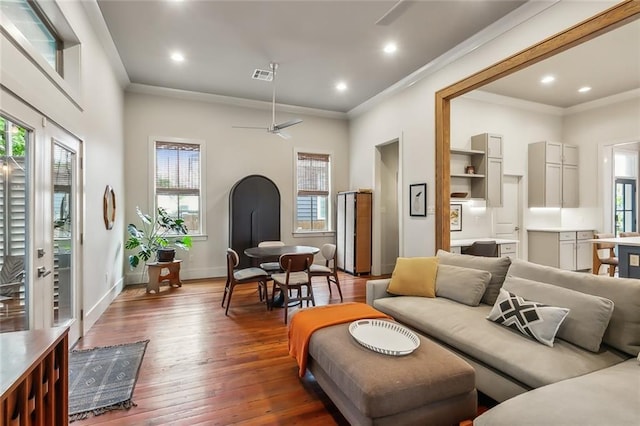 living area with wood-type flooring, visible vents, crown molding, and a healthy amount of sunlight