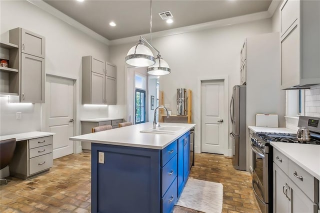 kitchen featuring brick floor, a sink, visible vents, appliances with stainless steel finishes, and a center island with sink