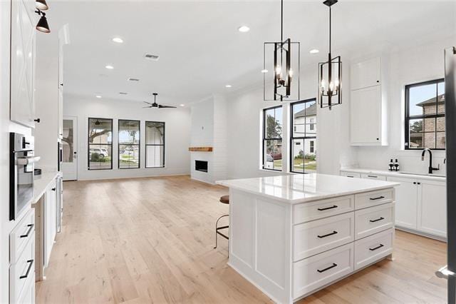 kitchen featuring a fireplace, a sink, white cabinets, light wood finished floors, and decorative light fixtures