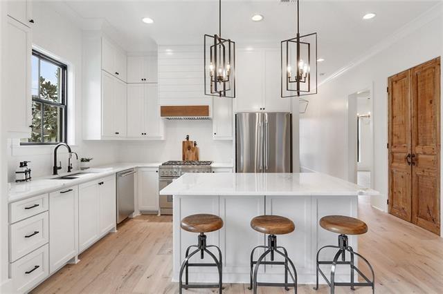 kitchen featuring stainless steel appliances, a sink, light wood-style floors, white cabinets, and a center island