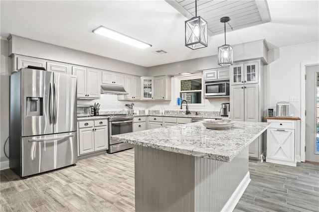 kitchen featuring light wood-style floors, glass insert cabinets, appliances with stainless steel finishes, light stone countertops, and under cabinet range hood