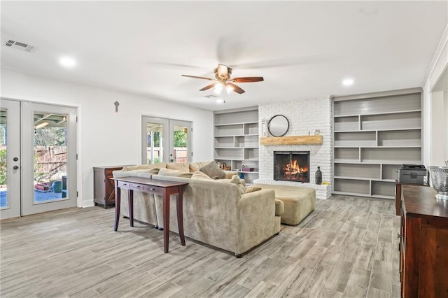 living room featuring light wood-style floors, a brick fireplace, french doors, and visible vents