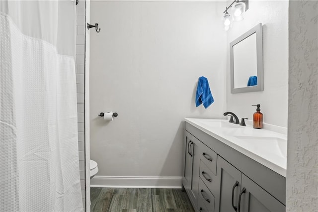 full bathroom featuring toilet, wood finished floors, a sink, baseboards, and double vanity