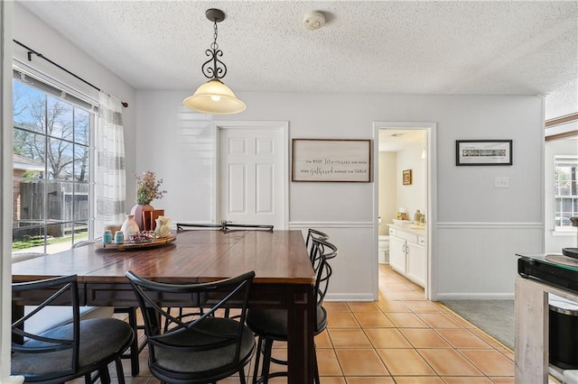 dining area featuring wainscoting, plenty of natural light, a textured ceiling, and light tile patterned floors