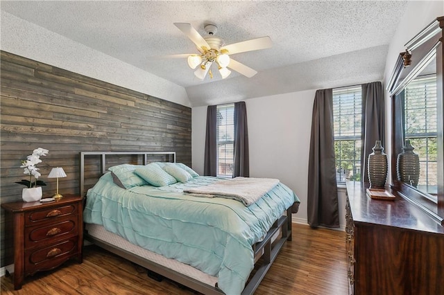 bedroom featuring lofted ceiling, wooden walls, a textured ceiling, wood finished floors, and baseboards