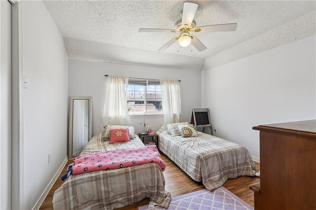 bedroom featuring ceiling fan, vaulted ceiling, a textured ceiling, wood finished floors, and baseboards