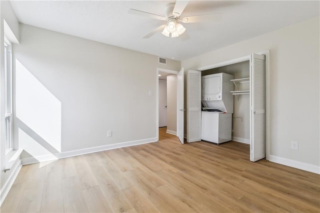 unfurnished bedroom with stacked washer and dryer, light wood-type flooring, visible vents, and baseboards