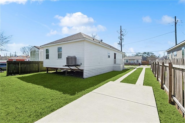 view of side of home with a shingled roof, central AC, a yard, and fence