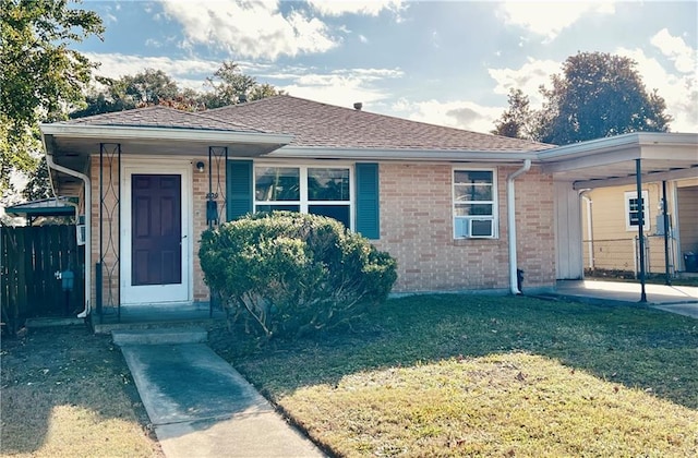 ranch-style home with an attached carport, fence, a shingled roof, a front lawn, and brick siding