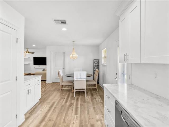 kitchen with visible vents, white cabinets, light wood-style flooring, light stone counters, and stainless steel dishwasher