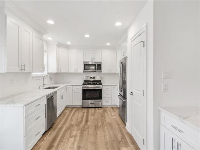 kitchen featuring light wood finished floors, appliances with stainless steel finishes, a sink, and white cabinets