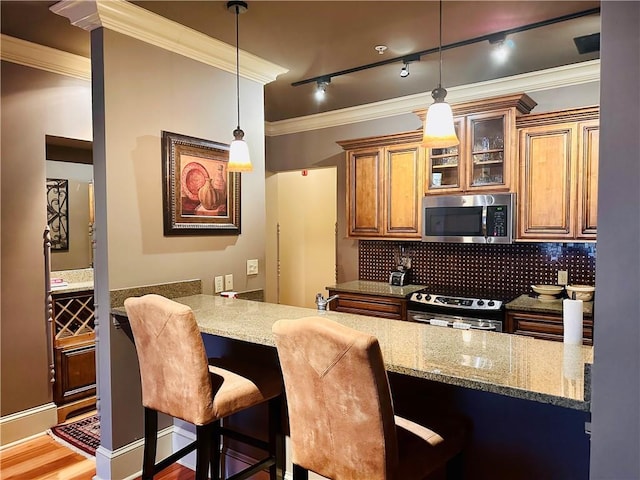 kitchen featuring brown cabinets, stainless steel appliances, decorative backsplash, ornamental molding, and light stone countertops