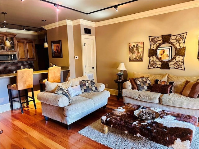 living area with rail lighting, visible vents, ornamental molding, wood finished floors, and baseboards