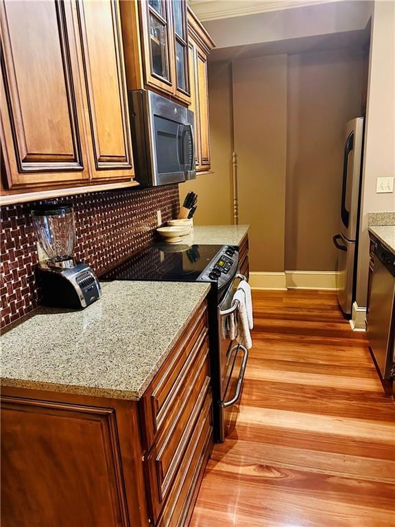 kitchen with light stone counters, stainless steel appliances, decorative backsplash, glass insert cabinets, and light wood-type flooring