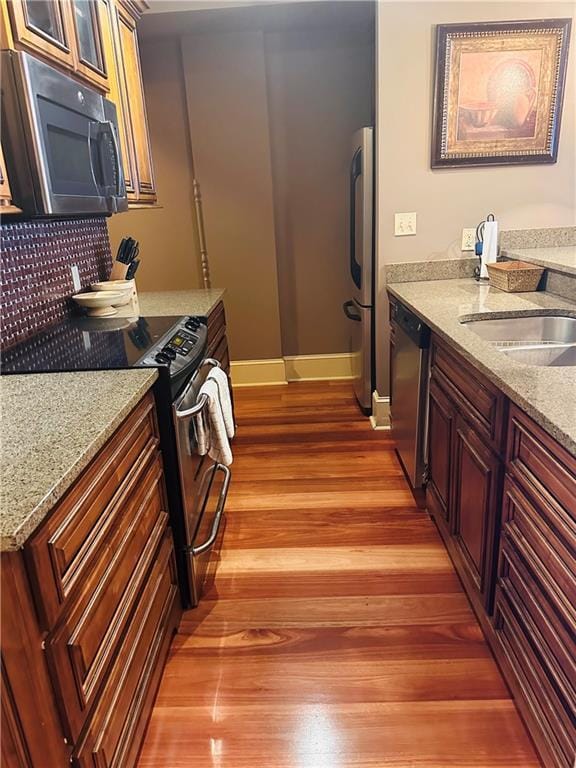 kitchen featuring light stone counters, stainless steel appliances, decorative backsplash, glass insert cabinets, and light wood-style floors