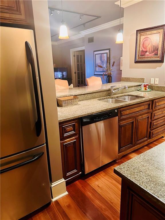 kitchen with dark wood-style flooring, a sink, appliances with stainless steel finishes, light stone countertops, and crown molding