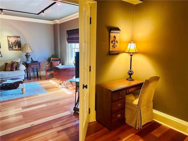 office space featuring rail lighting, baseboards, crown molding, and wood finished floors