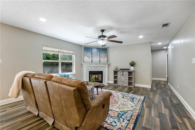 living room with a tiled fireplace, dark wood-type flooring, baseboards, and visible vents