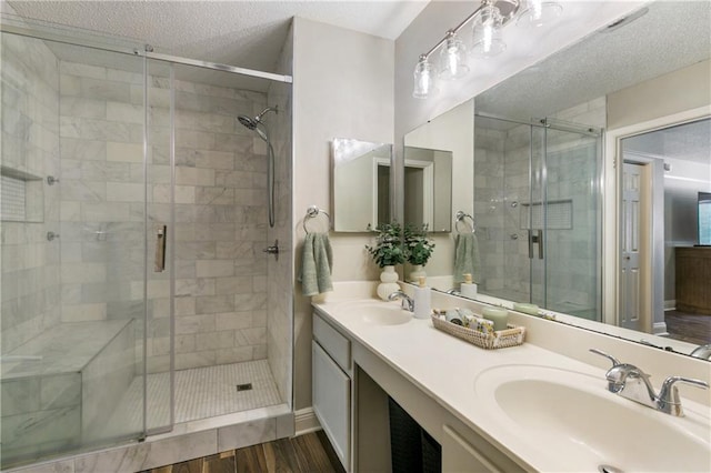 full bath with a textured ceiling, a shower stall, wood finished floors, and a sink