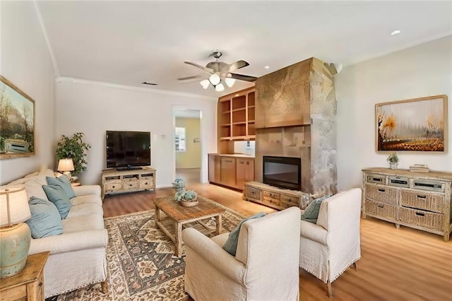 living area with ornamental molding, a fireplace, light wood-style flooring, and a ceiling fan