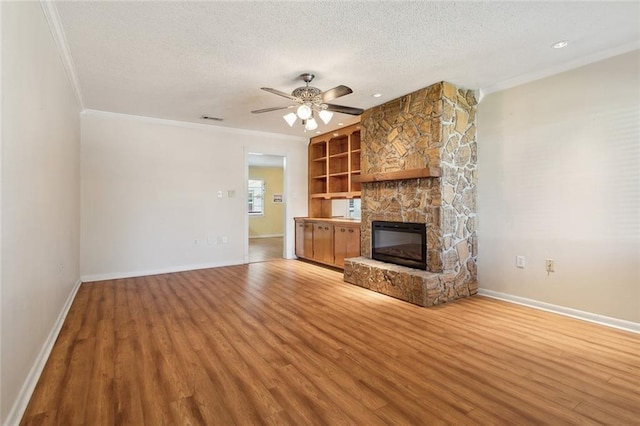 unfurnished living room with visible vents, light wood-style flooring, ornamental molding, a textured ceiling, and a fireplace