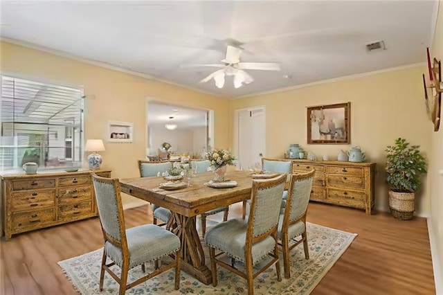 dining area with ornamental molding, light wood-type flooring, visible vents, and a ceiling fan