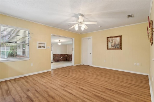 spare room featuring light wood-style floors, visible vents, ornamental molding, and a ceiling fan