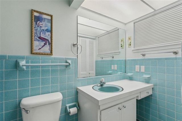 bathroom with toilet, a wainscoted wall, tile walls, and vanity