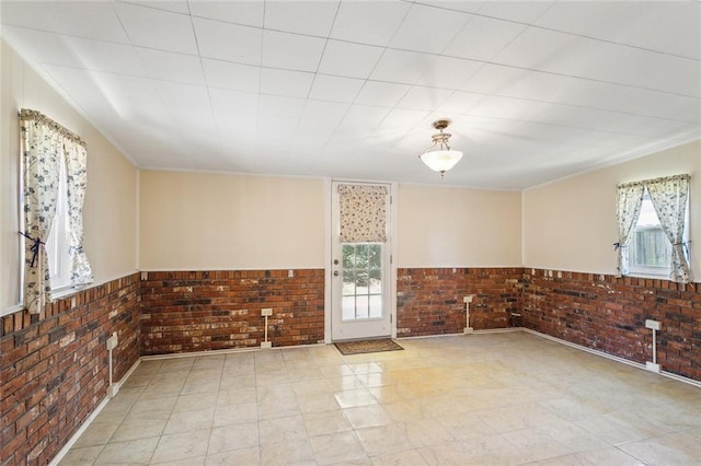 unfurnished room featuring a wainscoted wall, brick wall, and ornamental molding