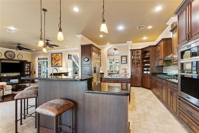 kitchen featuring visible vents, appliances with stainless steel finishes, open floor plan, a kitchen island, and a kitchen breakfast bar