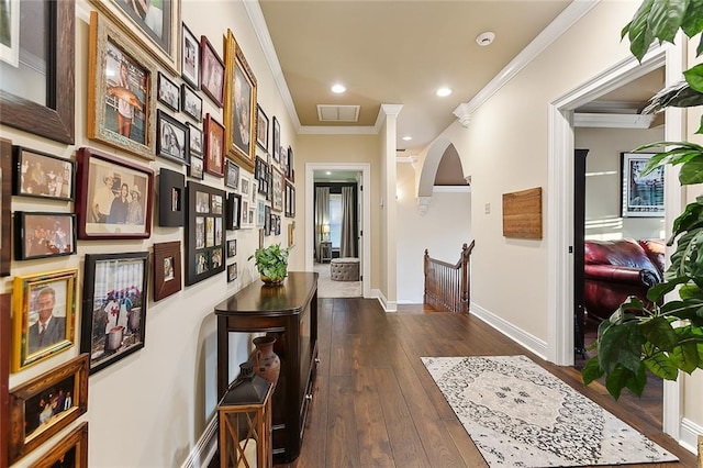 hallway featuring arched walkways, dark wood-type flooring, visible vents, baseboards, and crown molding