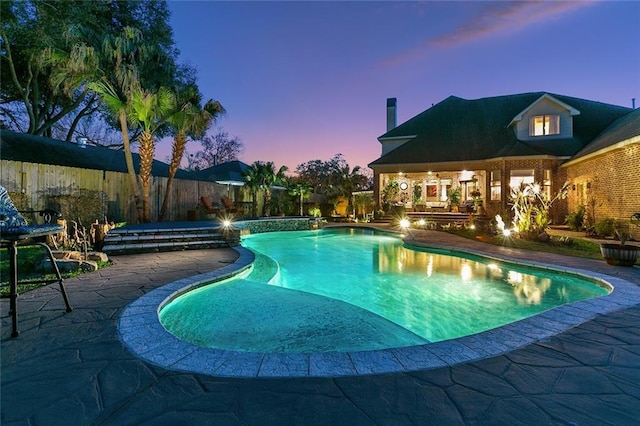 pool at dusk with a fenced backyard, a pool with connected hot tub, and a patio