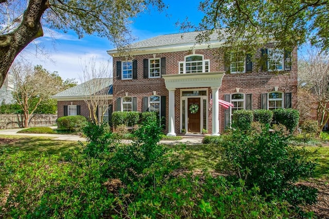 georgian-style home featuring a front yard, fence, and brick siding