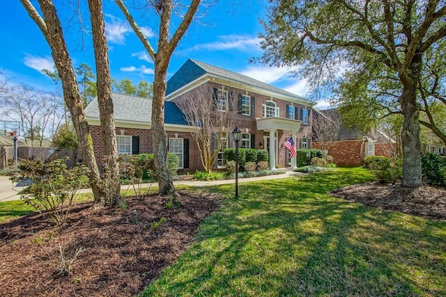 colonial house with brick siding, a front yard, and fence