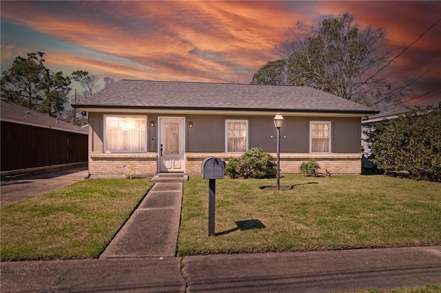 view of front facade featuring a shingled roof, brick siding, a yard, and stucco siding