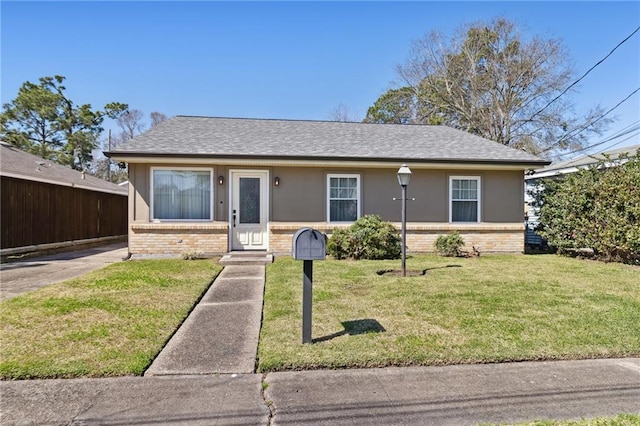 view of front of home with brick siding, a front yard, a shingled roof, and stucco siding