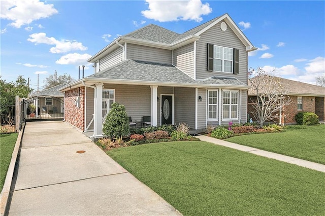 traditional home featuring driveway, roof with shingles, a gate, a front yard, and brick siding