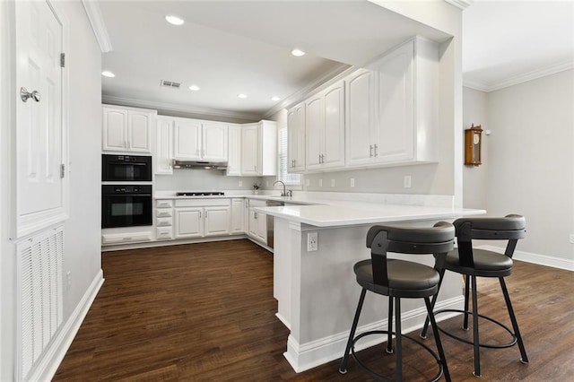 kitchen with visible vents, a breakfast bar area, ornamental molding, a peninsula, and under cabinet range hood