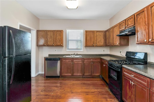 kitchen featuring dark wood finished floors, dark countertops, a sink, under cabinet range hood, and black appliances