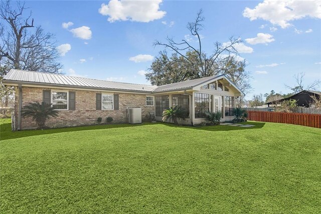 back of property with a lawn, fence, brick siding, and metal roof