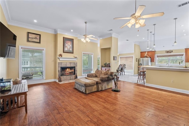 living area with a fireplace, visible vents, baseboards, ornamental molding, and light wood finished floors