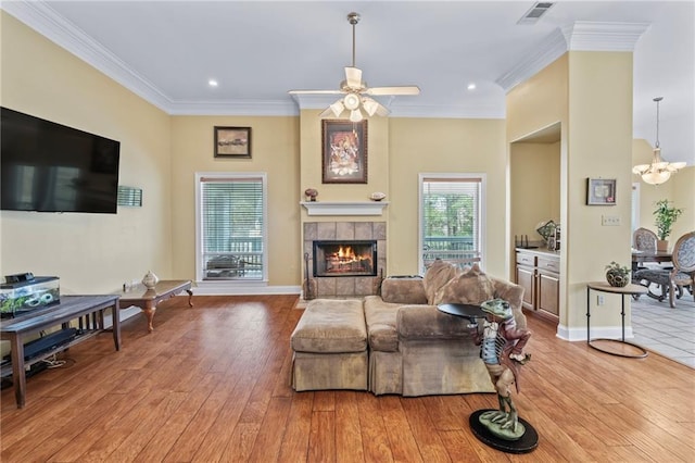 living room with crown molding, wood-type flooring, visible vents, a tile fireplace, and baseboards