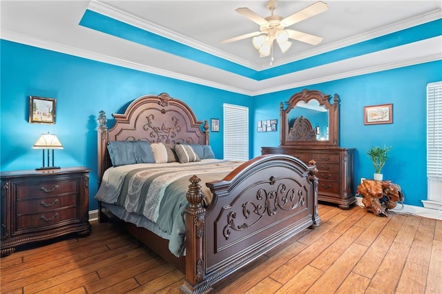 bedroom with a ceiling fan, a raised ceiling, hardwood / wood-style flooring, and crown molding