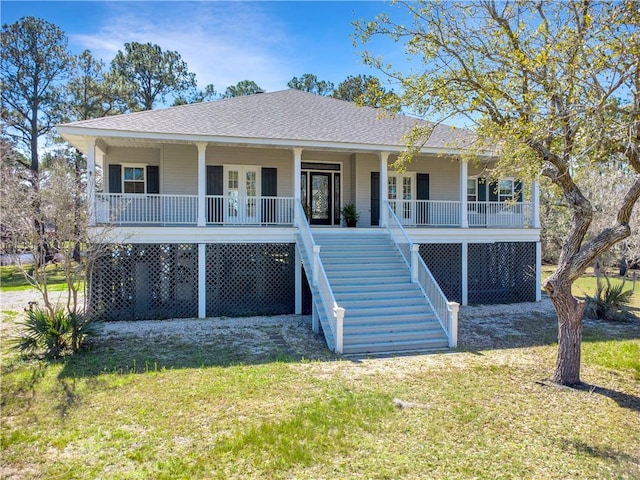 coastal home with covered porch, roof with shingles, stairs, and a front yard