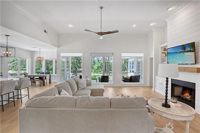 living area featuring a warm lit fireplace, built in shelves, plenty of natural light, and ornamental molding