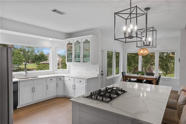 kitchen featuring visible vents, a kitchen island, appliances with stainless steel finishes, light stone counters, and a sink