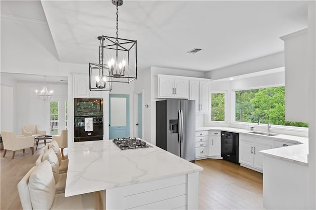 kitchen with visible vents, light stone counters, black appliances, white cabinetry, and a sink