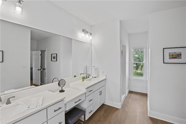 bathroom with double vanity, baseboards, a sink, and wood finished floors