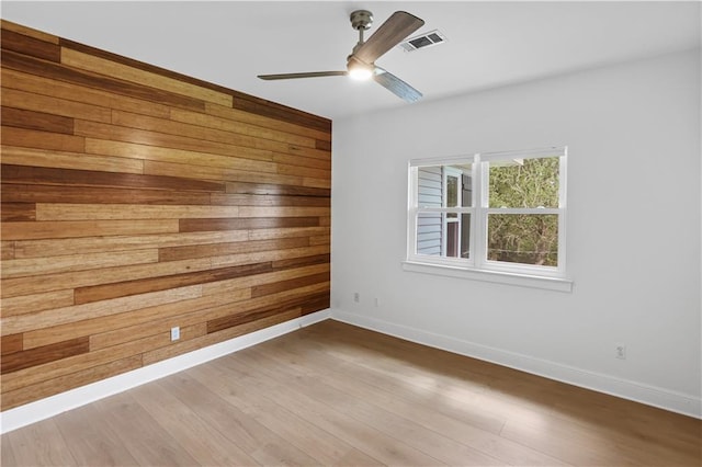 empty room with ceiling fan, wooden walls, visible vents, and wood finished floors