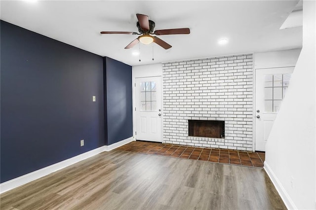 unfurnished living room with a ceiling fan, a brick fireplace, wood finished floors, and baseboards